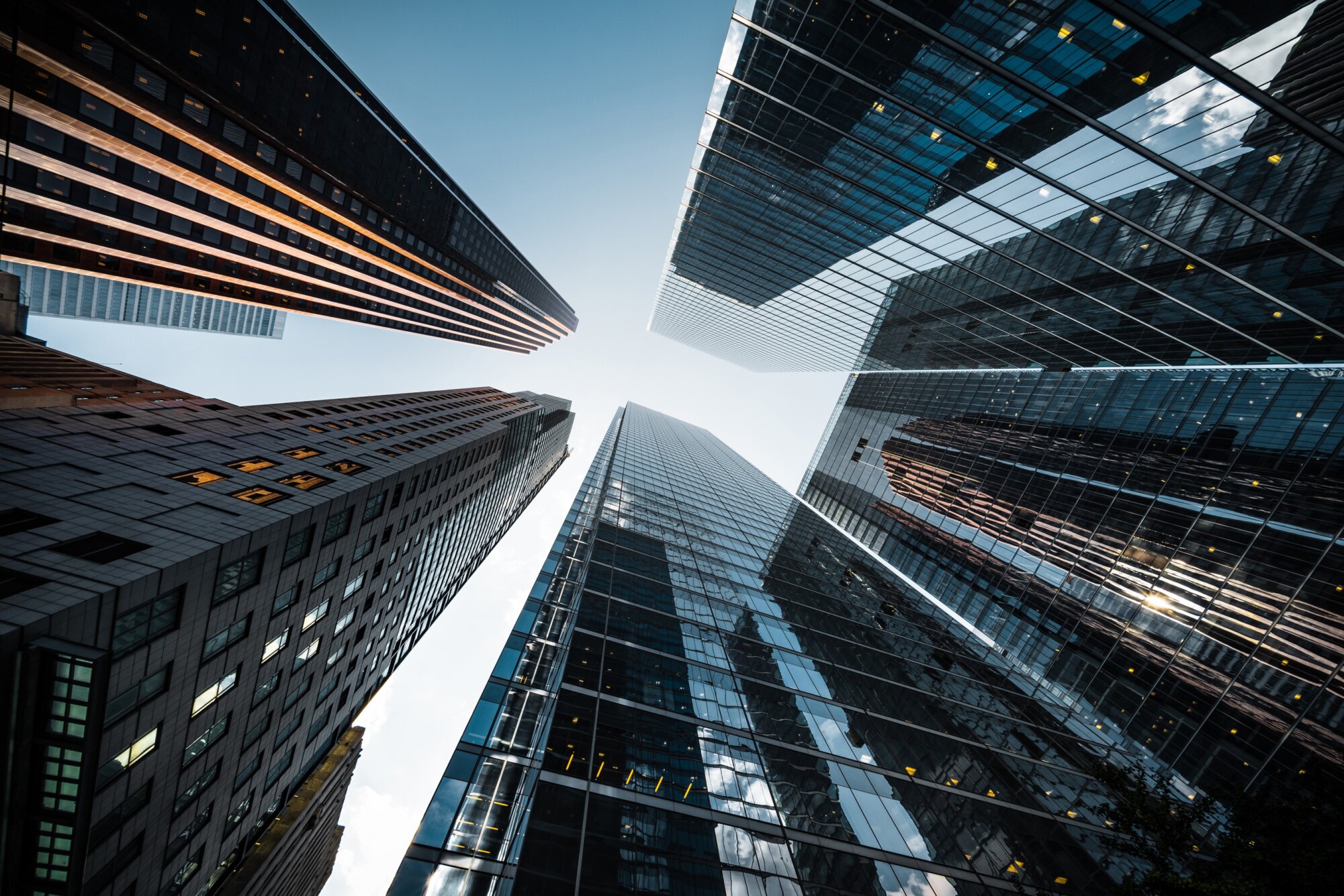 View from below of several tall glass skyscrapers converging towards the sky.