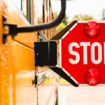 Side view of a school bus with an extended stop sign and two red lights.