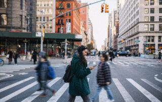 Woman crossing busy city street while looking at phone.