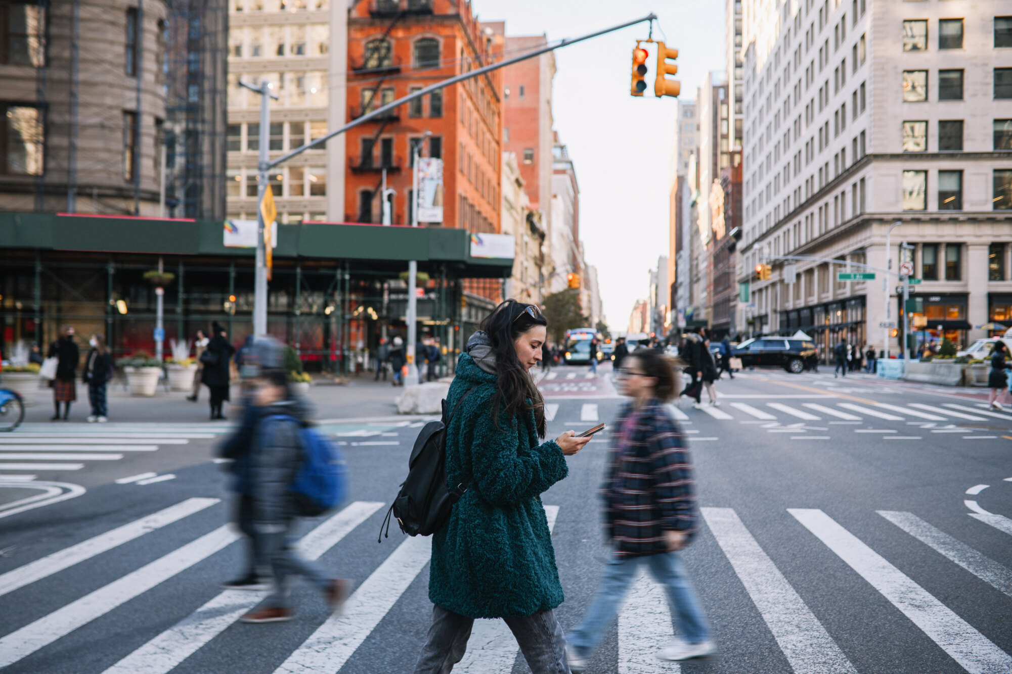 Woman crossing busy city street while looking at phone.