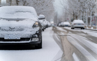 Snow-covered cars parked along a snowy, tree-lined street.